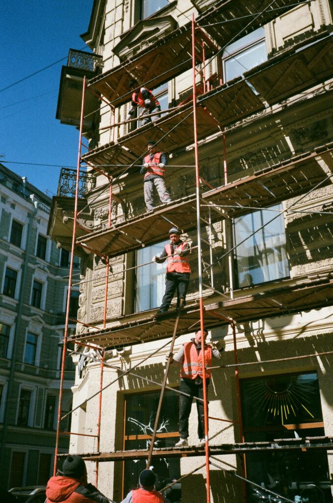 Construction workers on scaffolding renovating a building facade on a sunny day.